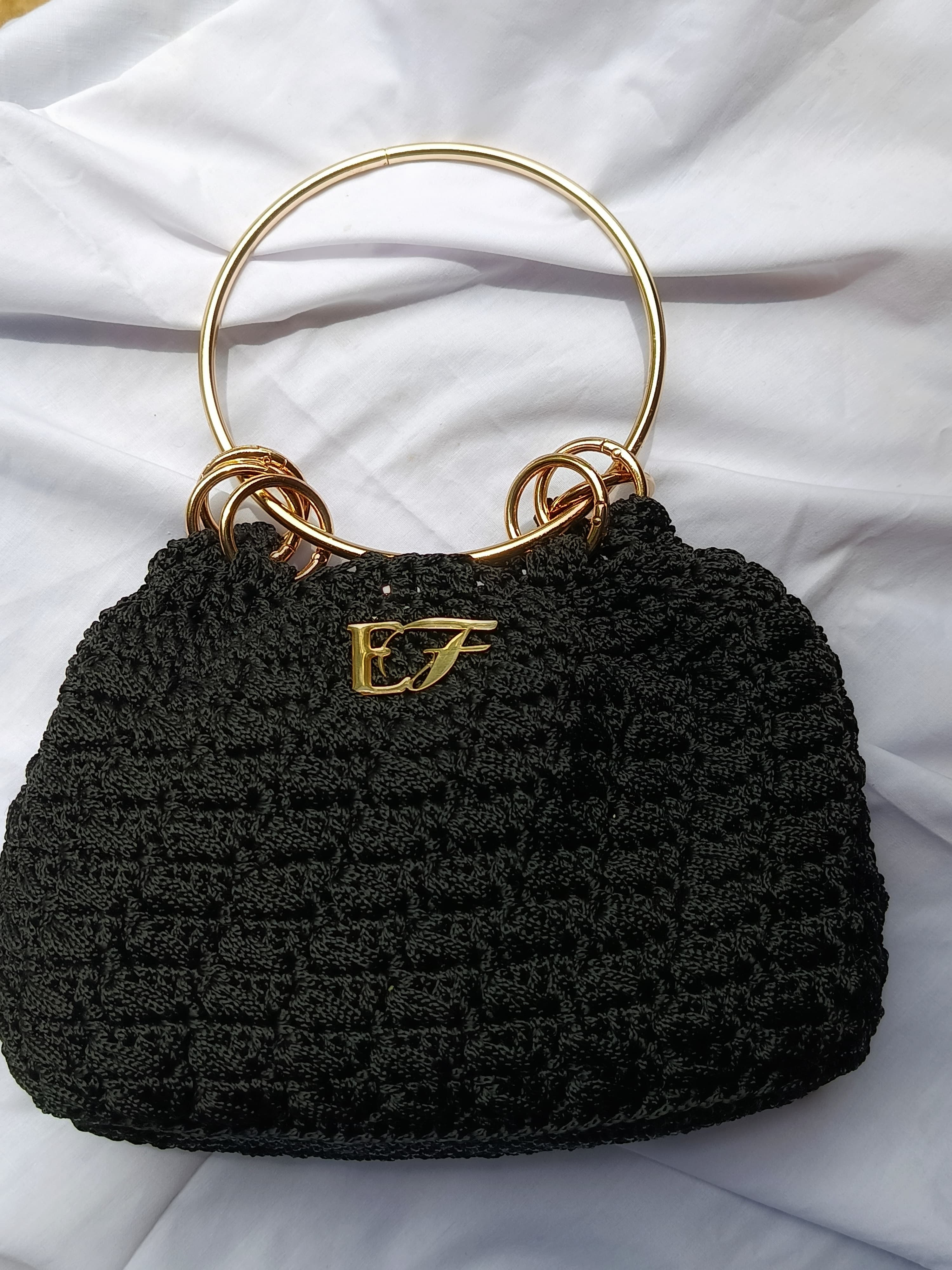 Onyx black crochet handbag with gold ring handle and EF emblem.
