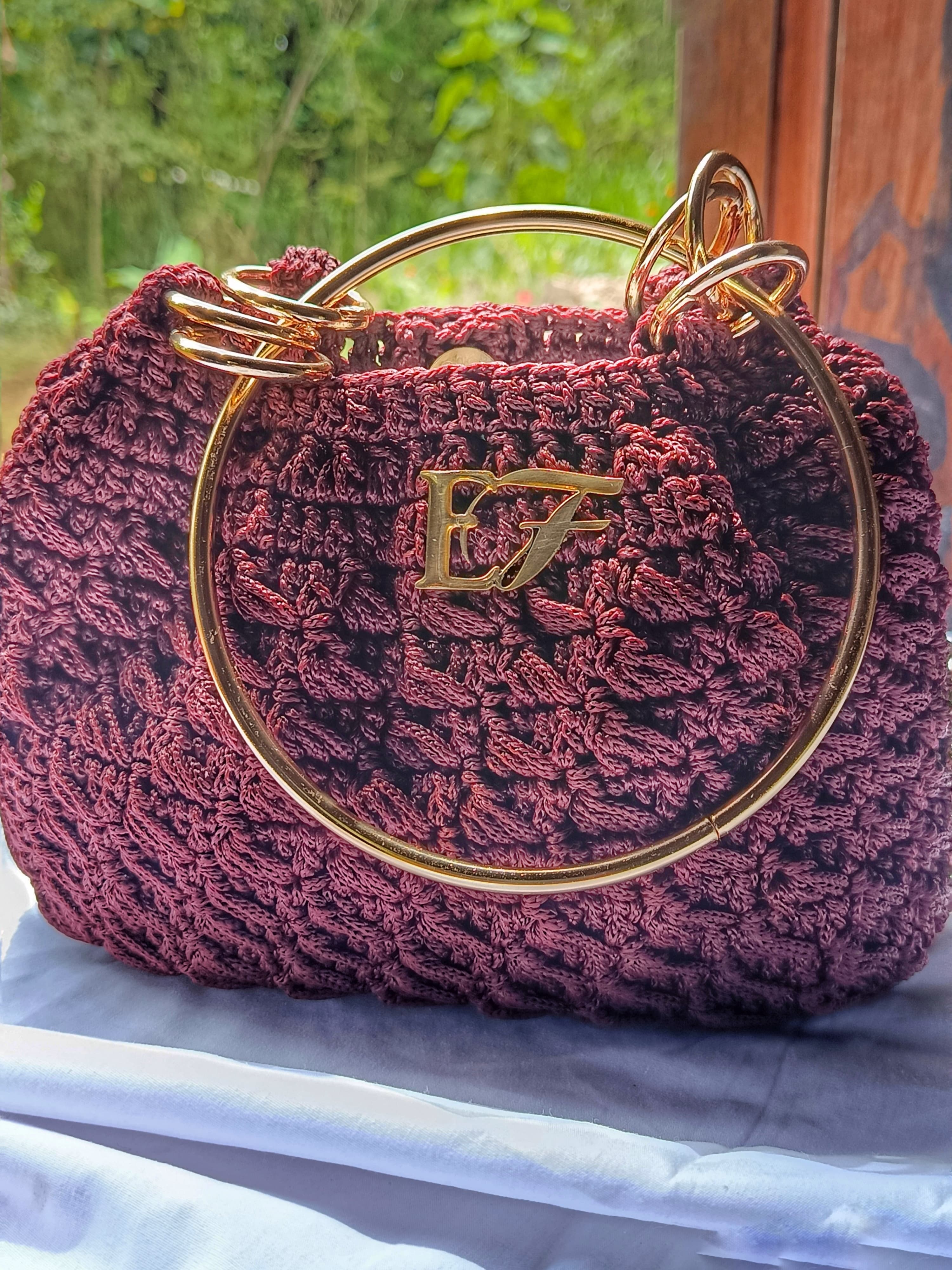 Wine-toned crochet handbag with gold ring handle and EF emblem.